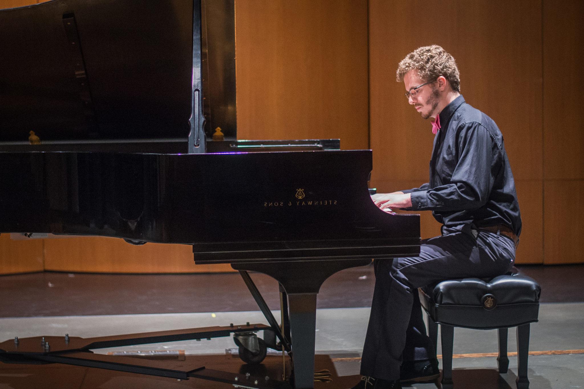 Student in black attire playing a grand piano on stage